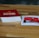 A wooden table features a stack of cards with a red cover labeled 'Exploding Kittens'. Next to it, a single card is laid out showing artwork and text related to the game. The setting is casual and likely related to a tabletop gaming session.
